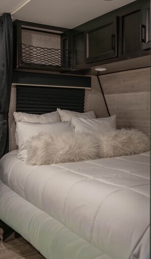 A bed with white bedding and a fluffy pillow, a dark headboard, and a window with a mesh screen. - Cozy Camper w/Pool · Cabo Rojo Lighthouse ·Combate (Boquerón)