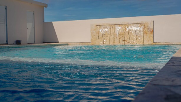 A swimming pool with clear blue water, a white wall, and a door in the background. - Cozy Camper w/Pool · Cabo Rojo Lighthouse ·Combate (Boquerón)