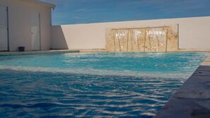En swimmingpool med klart, blåt vand, en hvid væg og en dør i baggrunden.