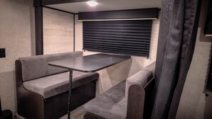 A compact RV interior with a small table and two cushioned seating areas. - Cozy Camper w/Pool · Cabo Rojo Lighthouse ·Combate (Boquerón)