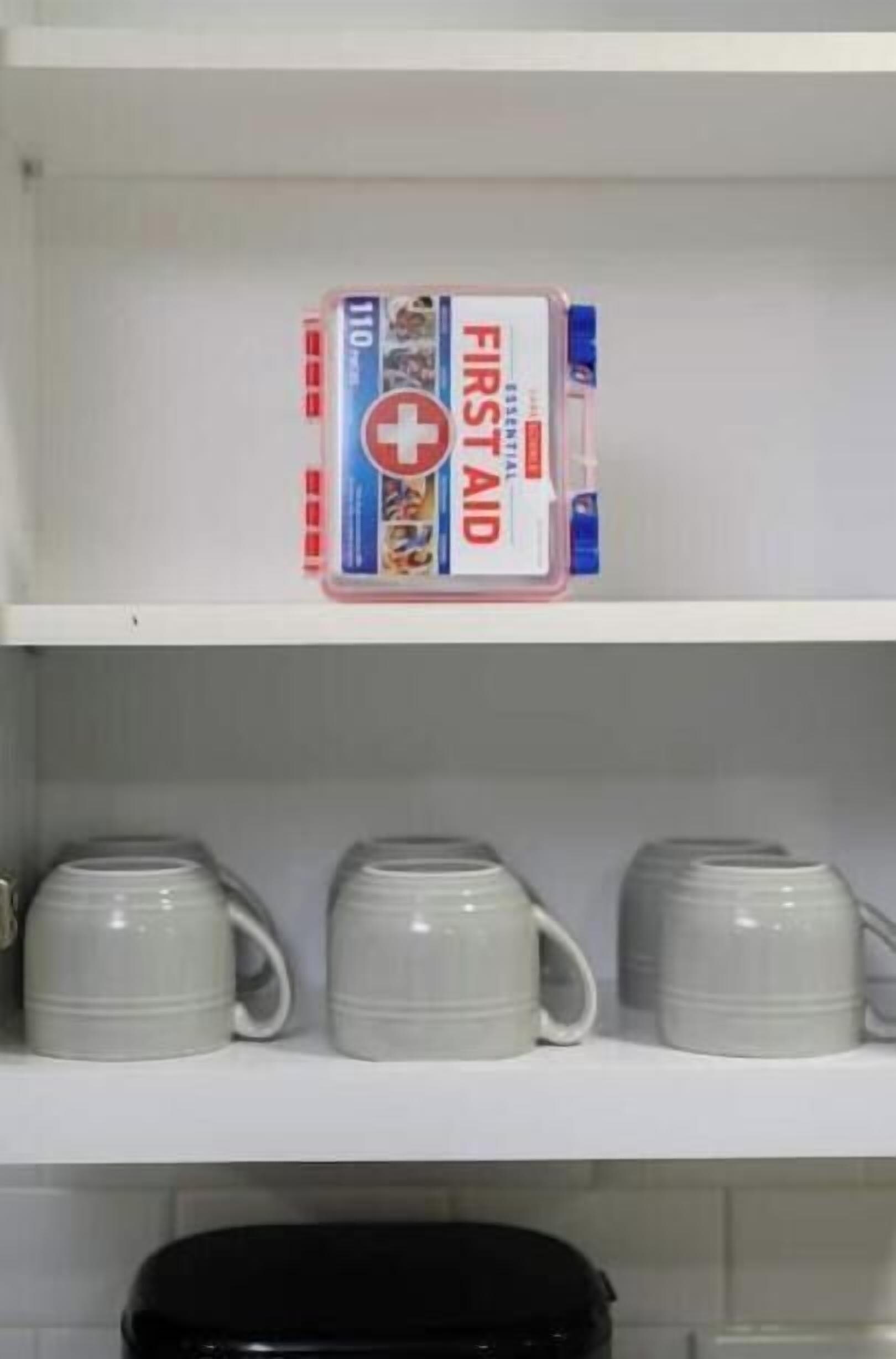 A shelf with a box of first aid kit and three white mugs.