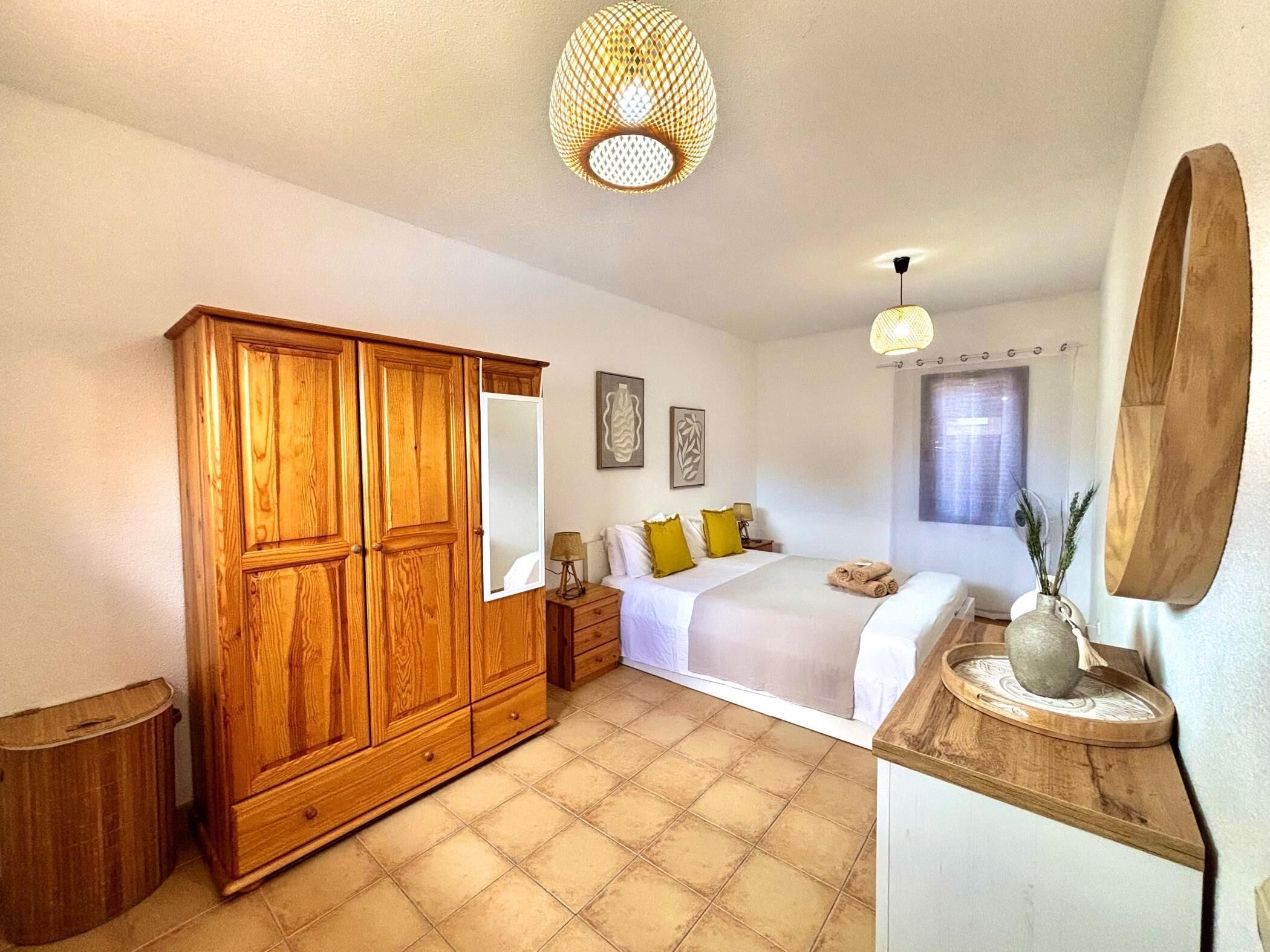 Ein Schlafzimmer mit einem Holzkleiderschrank, einem Bett mit weißer Bettwäsche, einem kleinen Nachttisch und einem Fenster mit Blick.