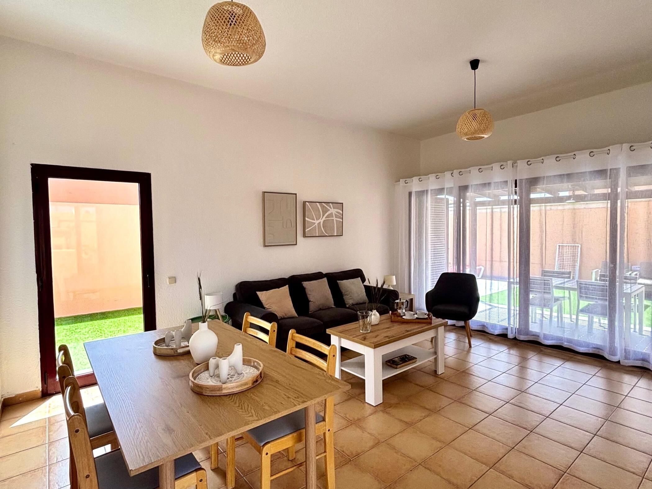 A living room with a sofa, coffee table, and chairs, a dining area with a table and chairs, and large windows with curtains.