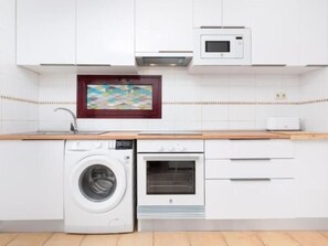 A kitchen with a washing machine, oven, microwave, and a framed picture on the wall. - Tajora House by Best Holidays Fuerteventura (Corralejo)