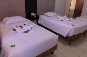 Een hotelkamer met drie keurig opgemaakte bedden, elk voorzien van witte lakens en decoratieve bloemstukken.