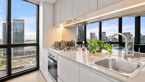 A modern kitchen with a large window, stainless steel appliances, and a view of the cityscape. - Docklands Marina Waterfront Luxury with 180° Views Pool, Gym & Carpark (Docklands)