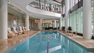 A modern indoor swimming pool with lounge chairs and a glass ceiling.