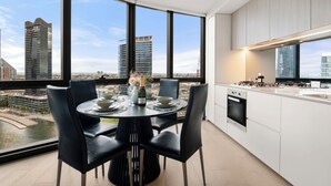 A modern kitchen with a large window, a dining area with a table set for four, and a view of the cityscape. - Docklands Marina Waterfront Luxury with 180° Views Pool, Gym & Carpark (Docklands)