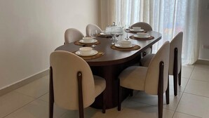 Un coin repas avec une table ronde dressée pour quatre personnes, six chaises, un luminaire au plafond et une fenêtre avec des rideaux.