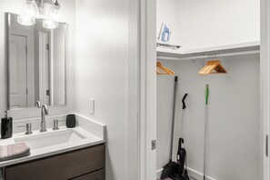 A bathroom with a white sink, mirror, and hanging clothes rack. - Modern & Cozy 1 Bedroom Apartment in Baton Rouge (Baton Rouge)
