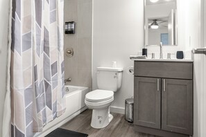 A bathroom with a toilet, bathtub, vanity, and a shower curtain. - Modern & Cozy 1 Bedroom Apartment in Baton Rouge (Baton Rouge)