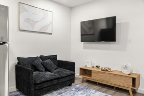 A modern living room with a sofa, a wooden TV stand, and a flat-screen TV mounted on the wall. - Modern & Cozy 1 Bedroom Apartment in Baton Rouge (Baton Rouge)