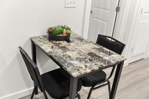 A small dining table with a black metal frame, two black chairs, and a potted plant on the table. - Modern & Cozy 1 Bedroom Apartment in Baton Rouge (Baton Rouge)