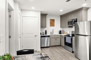 A modern kitchen with stainless steel appliances, light wood cabinets, and a white door. - Modern & Cozy 1 Bedroom Apartment in Baton Rouge (Baton Rouge)