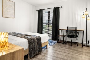 A hotel room with a bed, desk, chair, lamp, and window with curtains. - Modern & Cozy 1 Bedroom Apartment in Baton Rouge (Baton Rouge)