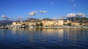 Un pueblo costero con un puerto deportivo, edificios y montañas al fondo.