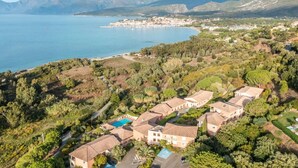 Vista aérea de una zona residencial costera con villas, piscina y vistas al mar y a las montañas.