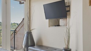 Een kamer met een aan de muur bevestigde televisie, een bankje en twee grote vazen met planten.