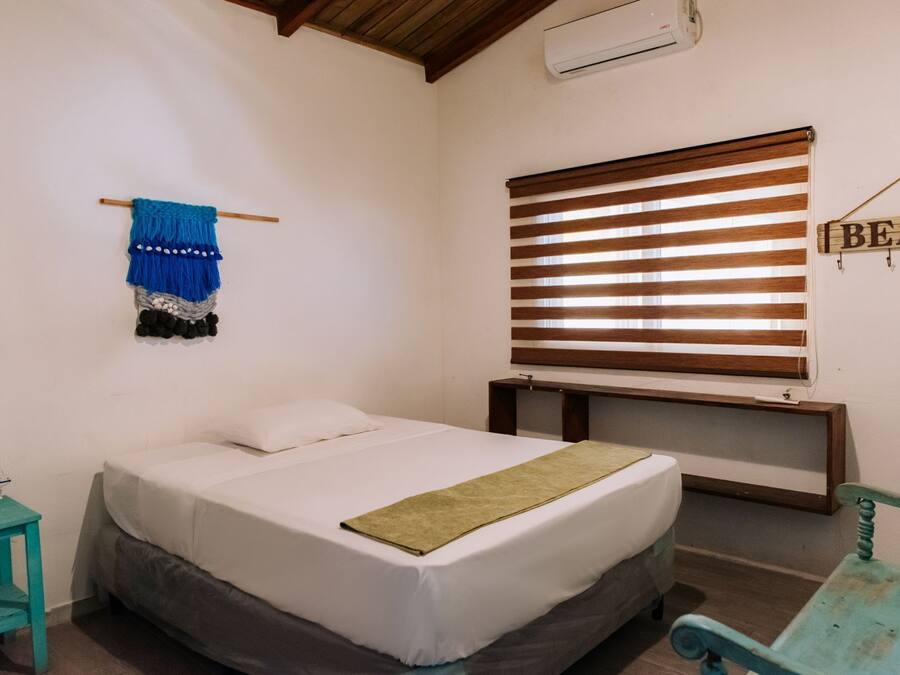 Une chambre à coucher comprenant un lit, une table de chevet, un climatiseur fixé au mur, une fenêtre avec des stores et un élément de décoration murale.
