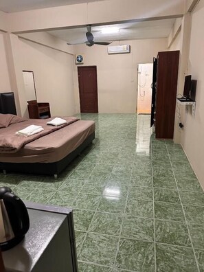 Ein Zimmer mit einem Bett, einem Schreibtisch, einem Stuhl, einem Deckenventilator und einer Tür.