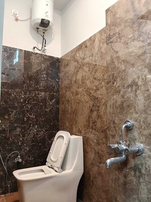Een badkamer met toilet, een in de muur gemonteerde douchekop en een marmeren wand.