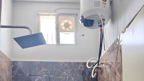 A bathroom with a bathtub, a showerhead, and a ceiling fan. - Deluxe Room (Tiruvannamalai)