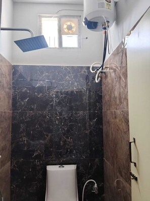 A bathroom with a bathtub, a showerhead, and a ceiling fan. - Deluxe Room (Tiruvannamalai)