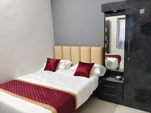 A hotel room with a bed, a bedside table with a phone, a mirror, and a wardrobe. - Deluxe Room (Tiruvannamalai)