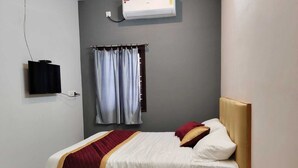 A single bed with a wooden headboard, a red and white bedspread, and two pillows. There is a wall-mounted air conditioner above the bed and a television on the left. - Deluxe Room (Tiruvannamalai)