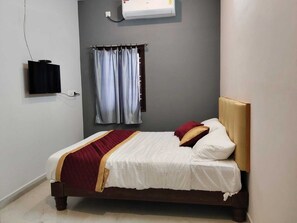 A single bed with a wooden headboard, a red and white bedspread, and two pillows. There is a wall-mounted air conditioner above the bed and a television on the left. - Deluxe Room (Tiruvannamalai)