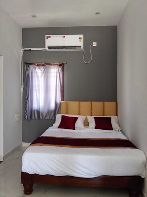 A single bed with a wooden frame, a headboard, and a white bedspread. - Deluxe Room (Tiruvannamalai)