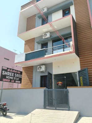 A multi-story building with balconies, air conditioning units, and a signboard advertising a home stay. - Deluxe Room (Tiruvannamalai)