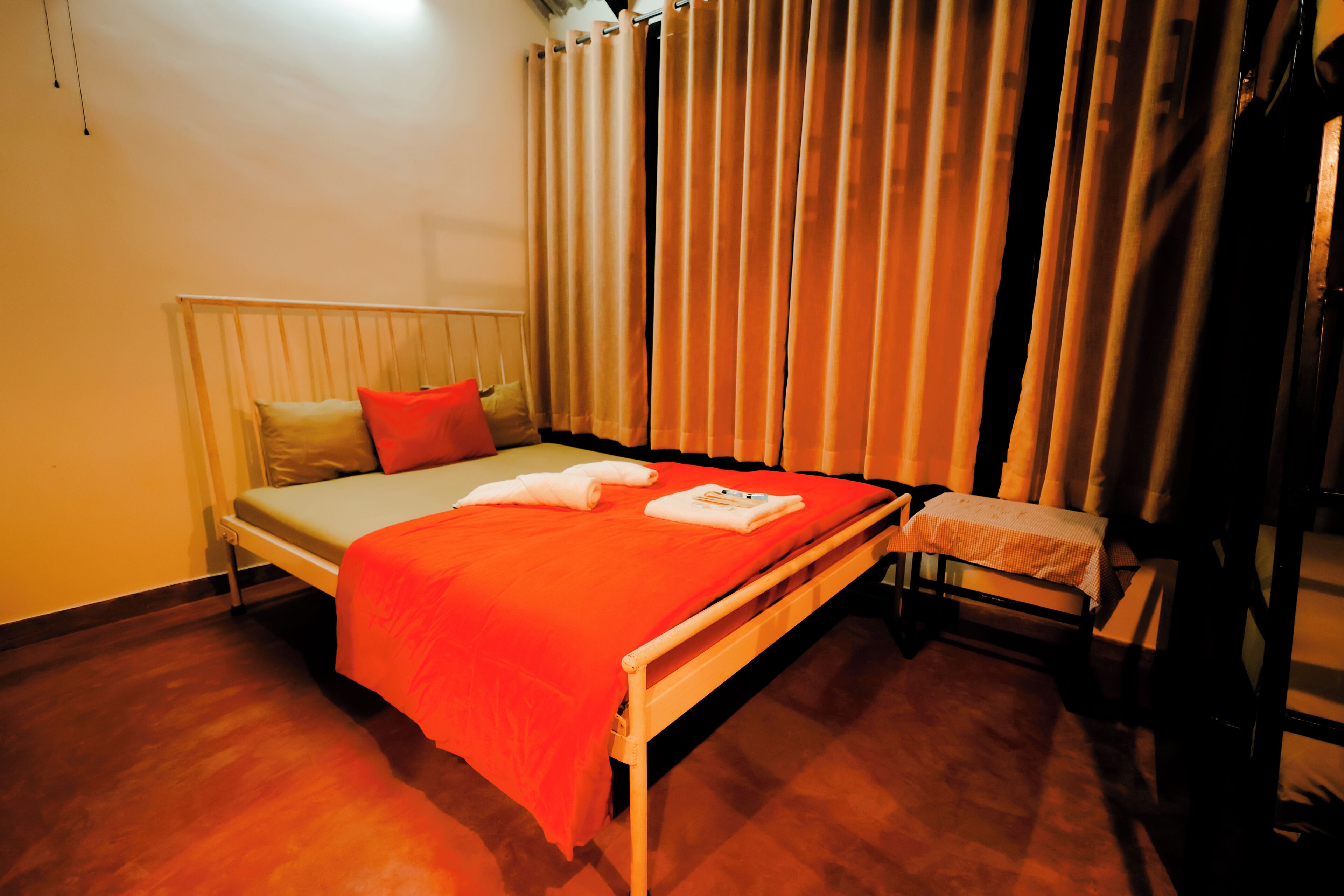 Una cama individual con colcha naranja, cabecera blanca y almohada roja.