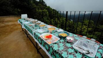 Mesa servida con diferentes platos y utensilios, rodeada por una barandilla con vista al bosque.