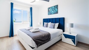 Ein modernes Schlafzimmer mit Bett, Deckenventilator, Nachttisch und einem Fenster mit Vorhängen.