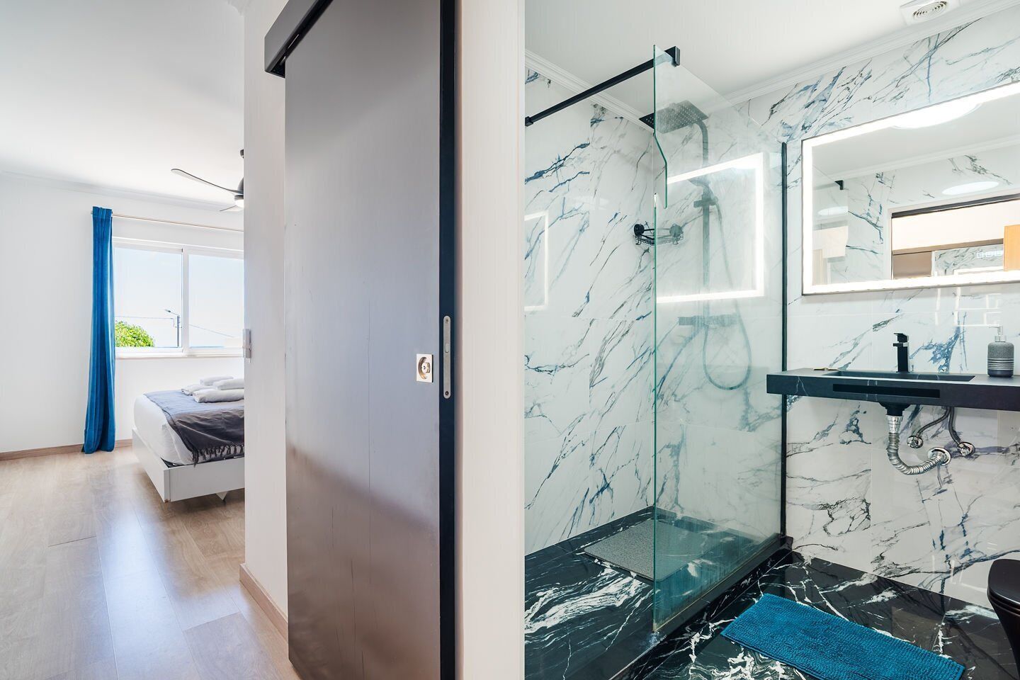A modern bathroom with a glass shower enclosure, a marble-tiled wall, and a built-in sink.
