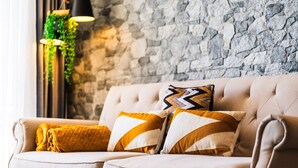 Ein beiges Sofa mit gemusterten Kissen, eine Steinwand und hängende Pflanzen.