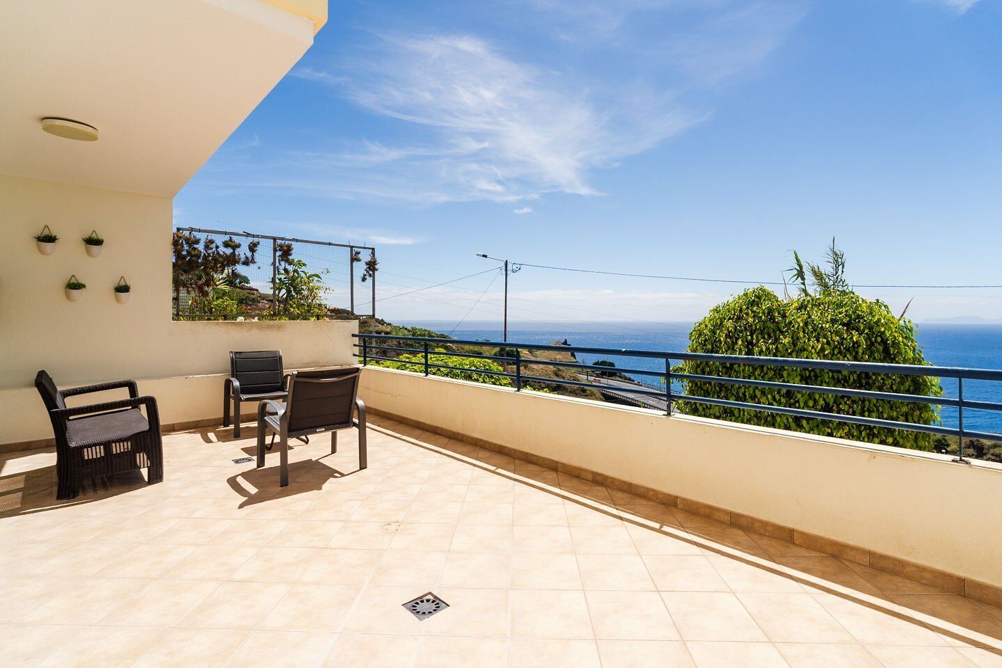 A balcony with a view of the sea, a table with chairs, and potted plants.