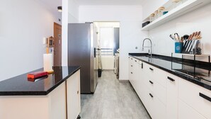 Eine moderne Küche mit einem Edelstahlkühlschrank, weißen Schränken, schwarzen Arbeitsflächen und einer eingebauten Ablage mit Küchenutensilien.