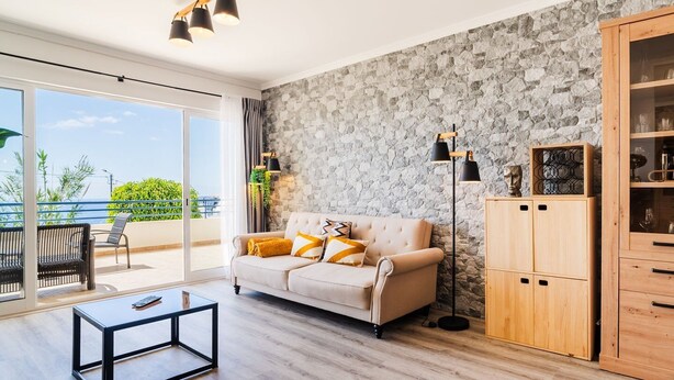 Ein Wohnzimmer mit einer Couch, einem Couchtisch, einer Steinsäule, einer Holzeinrichtung und Blick durch eine Glastür.