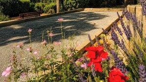 Een tuin met een grindpad, banken en verschillende bloeiende planten.