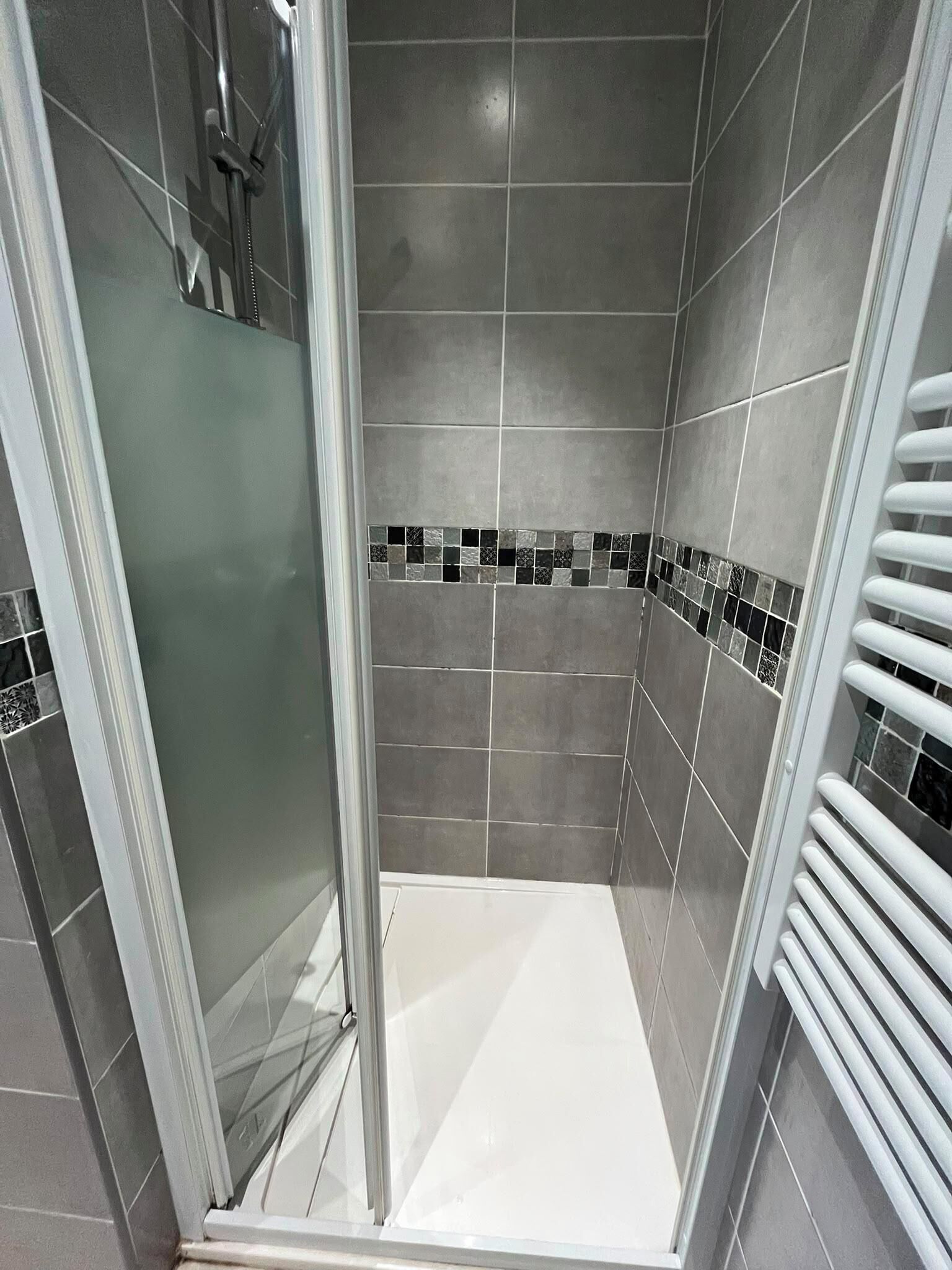 Une douche avec une porte en verre, des murs carrelés et un sol blanc.