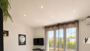 Een moderne woonkamer met een houten tafel, een bank, een flatscreen televisie en een groot raam met gordijnen.