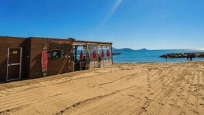 Een gebouw aan het strand met een houten gevel, een surfplank en rode parasols.