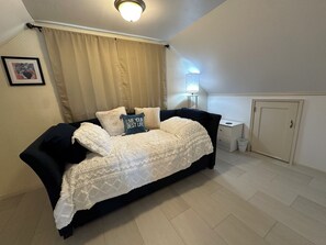 Quarto com cama, mesa de cabeceira, abajur, porta e quadro na parede.