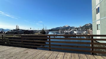 Una terraza de madera con vista a un puerto deportivo y montañas al fondo.