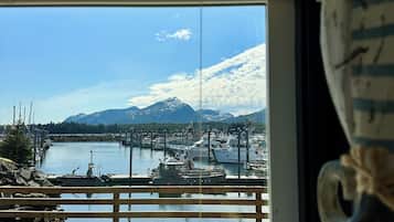 Una terraza de madera con vista a un puerto deportivo, barcos y montañas.