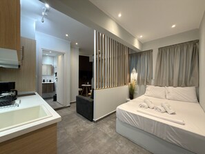 A modern hotel room with a bed, a desk, a kitchenette, and a bathroom. - SmartLiving Central Apt 5 (Thessaloniki)