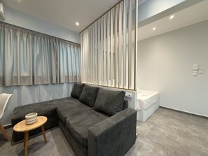 A modern living room with a sectional sofa, a small wooden table, and a bed in the background. - SmartLiving Central Apt 5 (Thessaloniki)
