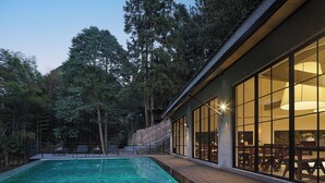 A swimming pool with a wooden deck, surrounded by tall trees and a building with large windows. - Zhangjiajie national park Oxgen Resort (Zhangjiajie)